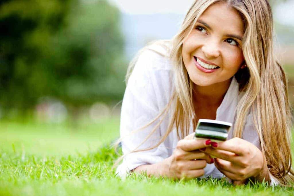 Smiling-woman-in-grass-typing-on-phone