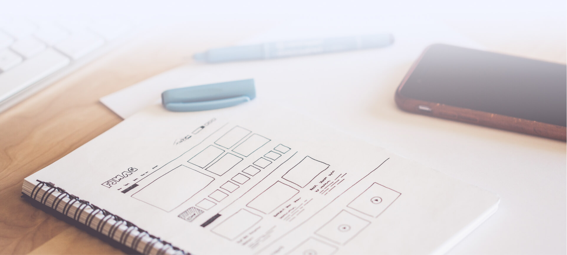 A desk with a notebook, pen, and cell phone for UX/UI work.