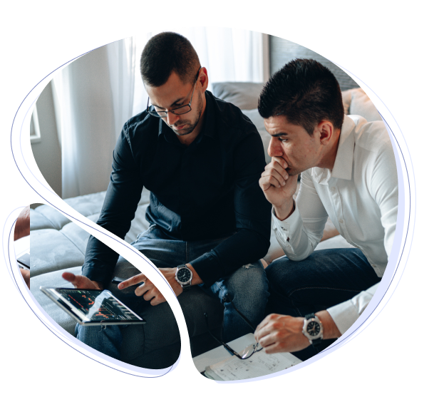 two men sitting on a couch looking at a laptop.